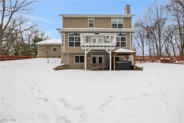 snow covered rear of property with a jacuzzi and a deck