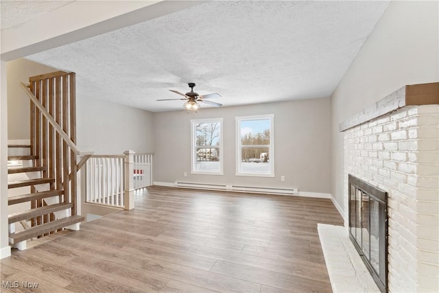 unfurnished living room with hardwood / wood-style floors, ceiling fan, baseboard heating, a brick fireplace, and a textured ceiling