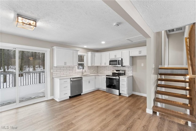 kitchen with sink, light wood-type flooring, white cabinets, and appliances with stainless steel finishes