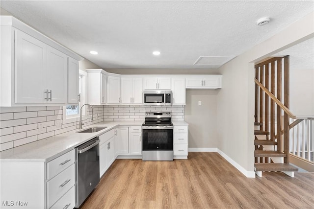 kitchen with appliances with stainless steel finishes, sink, white cabinets, and light hardwood / wood-style flooring