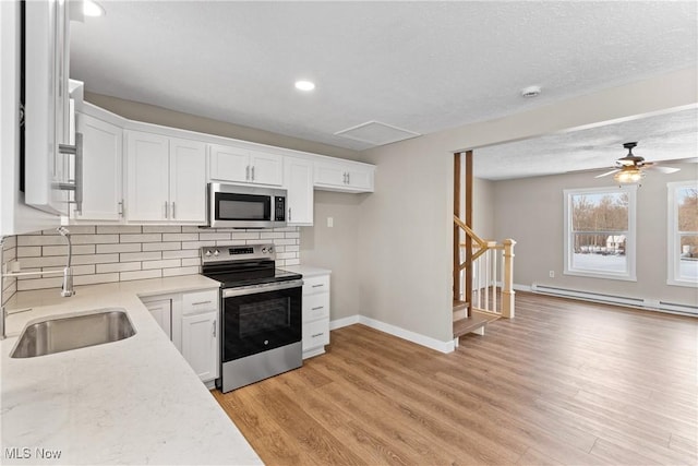 kitchen with baseboard heating, stainless steel appliances, light hardwood / wood-style floors, decorative backsplash, and white cabinets