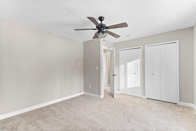 unfurnished bedroom with ceiling fan, a textured ceiling, light carpet, and two closets