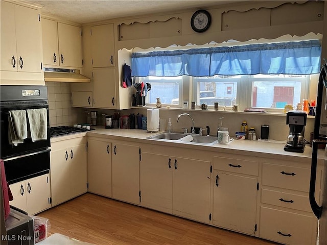 kitchen featuring tasteful backsplash, sink, black oven, and light wood-type flooring