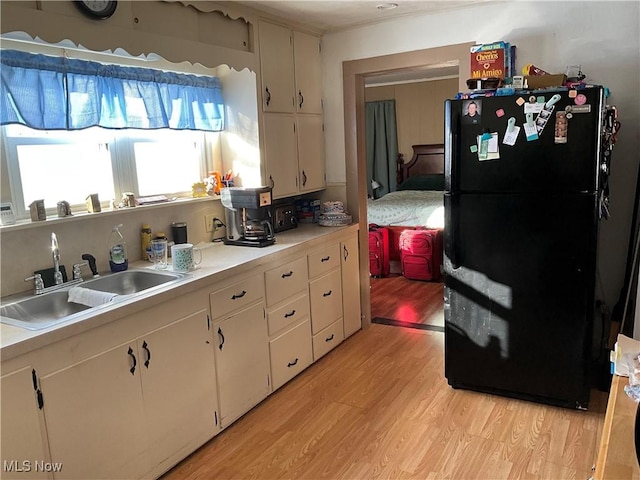 kitchen with black refrigerator, sink, white cabinetry, and light wood-type flooring