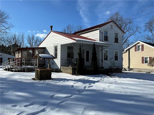 snow covered rear of property featuring a sunroom