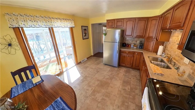 kitchen with stainless steel refrigerator, decorative backsplash, sink, and electric range oven