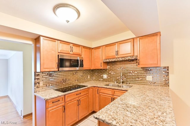 kitchen with light stone countertops, sink, black electric cooktop, and decorative backsplash