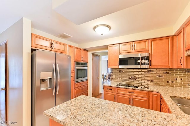 kitchen with backsplash, light stone countertops, kitchen peninsula, and appliances with stainless steel finishes