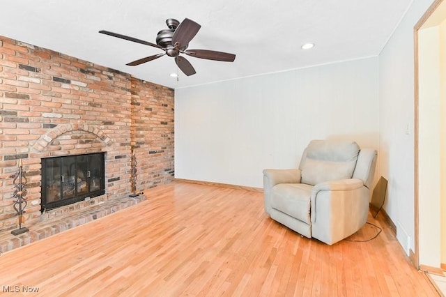 living area with ceiling fan, a brick fireplace, and light hardwood / wood-style floors