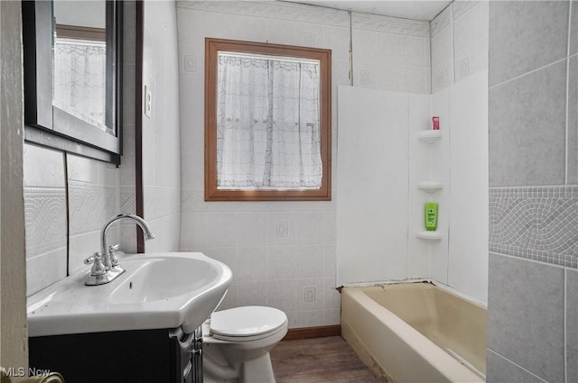 bathroom with a tub to relax in, toilet, tile walls, vanity, and hardwood / wood-style floors