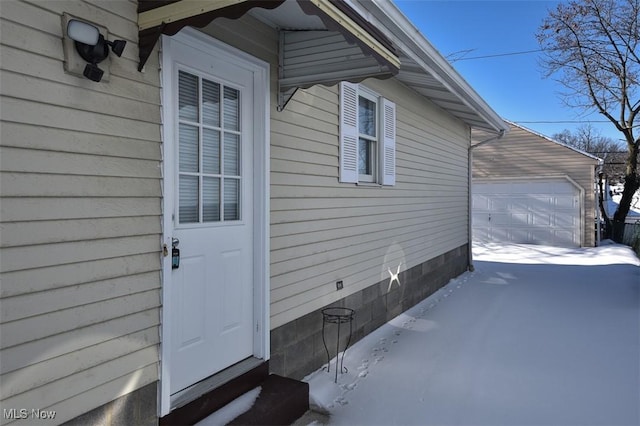 view of snowy exterior featuring a garage and an outbuilding