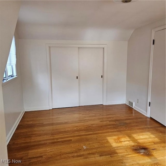 unfurnished bedroom with wood-type flooring, vaulted ceiling, and a closet