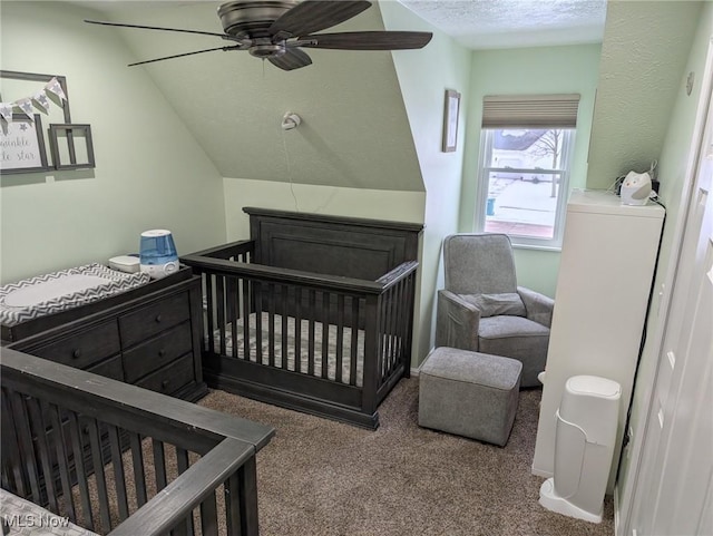 bedroom with lofted ceiling, ceiling fan, a nursery area, carpet floors, and a textured ceiling