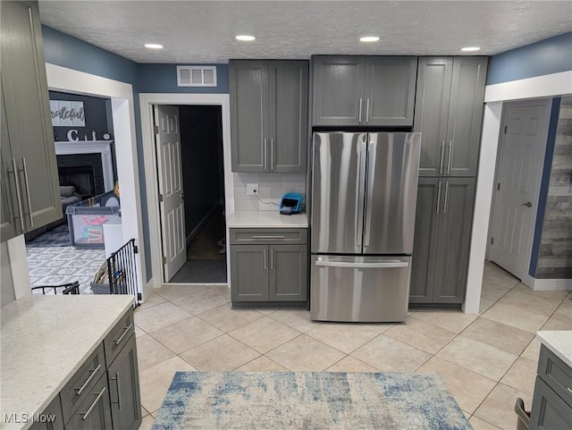 kitchen with gray cabinetry, a textured ceiling, stainless steel refrigerator, and light tile patterned floors