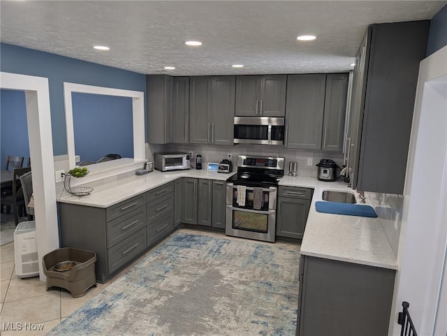 kitchen with gray cabinets, stainless steel appliances, a textured ceiling, light tile patterned flooring, and decorative backsplash