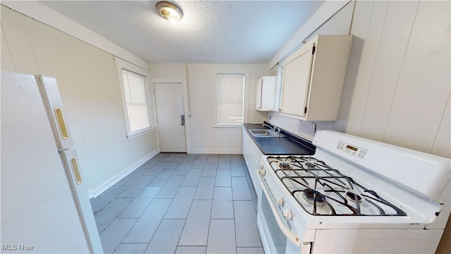 kitchen featuring sink, wood walls, a textured ceiling, white appliances, and white cabinets