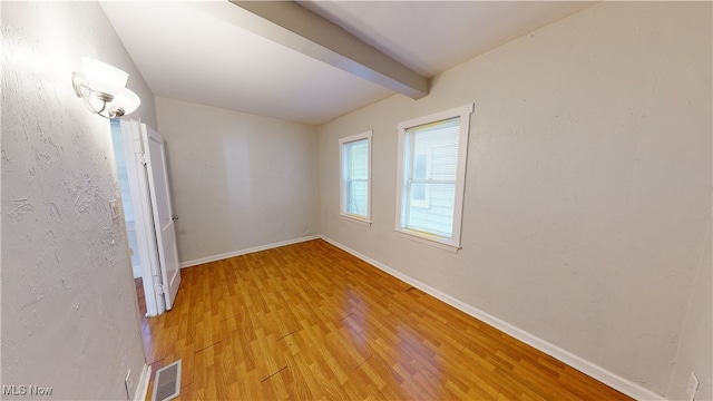 spare room featuring wood-type flooring and beam ceiling