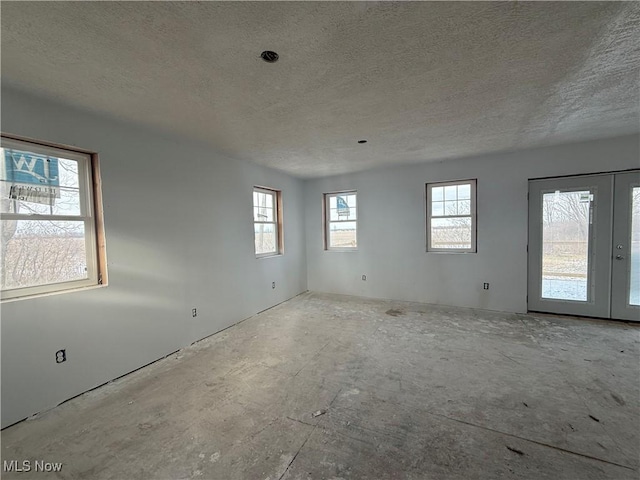 empty room featuring a textured ceiling, french doors, and a healthy amount of sunlight