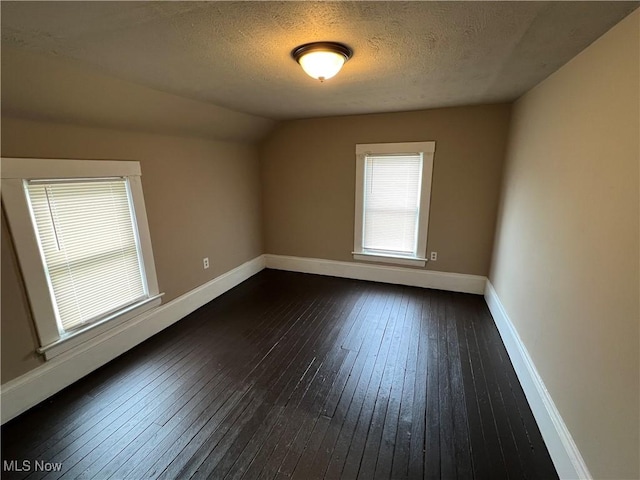 empty room featuring lofted ceiling, dark hardwood / wood-style flooring, and a textured ceiling