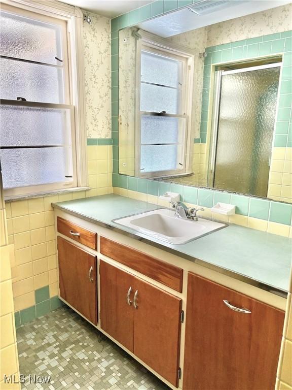 bathroom with walk in shower, plenty of natural light, tile walls, and vanity