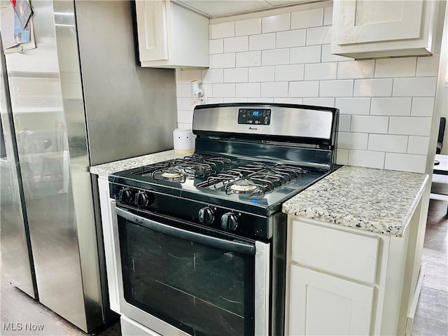 kitchen featuring white cabinetry, light stone countertops, stainless steel gas range, and backsplash