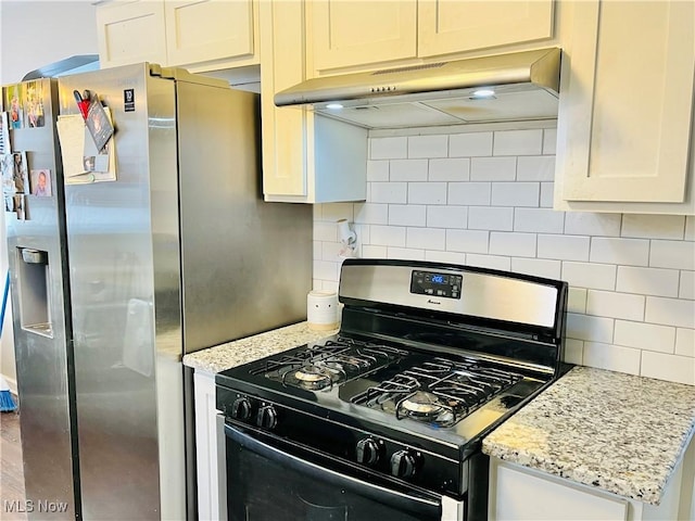 kitchen with black range with gas cooktop, stainless steel fridge, light stone countertops, decorative backsplash, and white cabinets