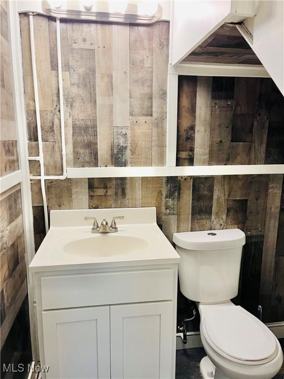 bathroom with vanity, toilet, and wood walls