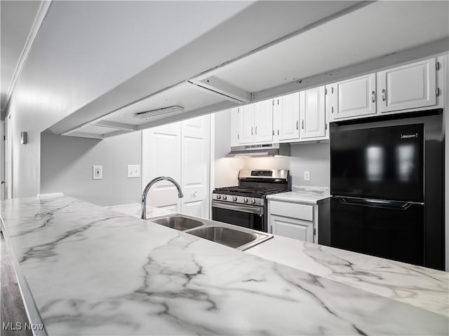 kitchen with sink, black refrigerator, stainless steel gas stove, white cabinetry, and light stone counters