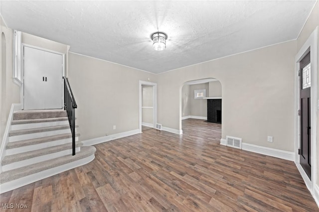 unfurnished living room with dark wood-type flooring, a brick fireplace, and a textured ceiling