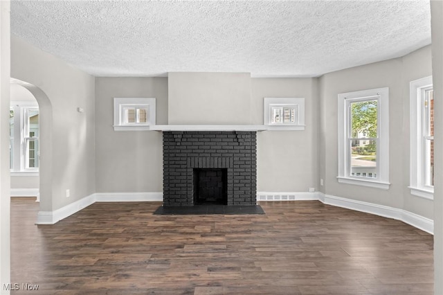 unfurnished living room featuring a brick fireplace, a textured ceiling, and dark hardwood / wood-style flooring