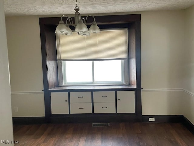 unfurnished dining area featuring dark hardwood / wood-style floors, a chandelier, and a textured ceiling