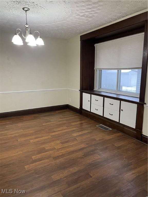 spare room featuring an inviting chandelier, dark hardwood / wood-style floors, and a textured ceiling