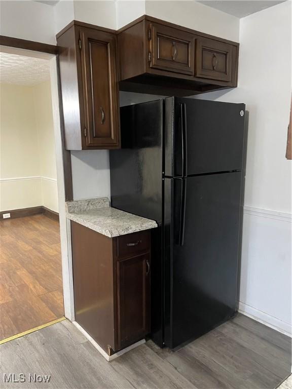 kitchen with dark brown cabinets, black refrigerator, and light hardwood / wood-style flooring