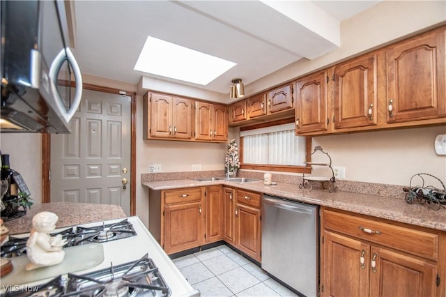 kitchen featuring stainless steel appliances, sink, light tile patterned floors, and a skylight