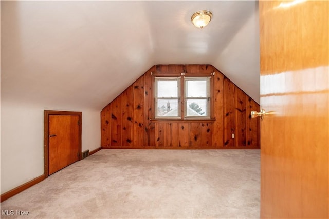 bonus room with vaulted ceiling, light colored carpet, and wood walls