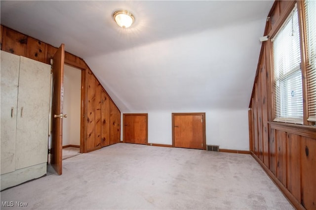 bonus room with vaulted ceiling, light carpet, and wood walls