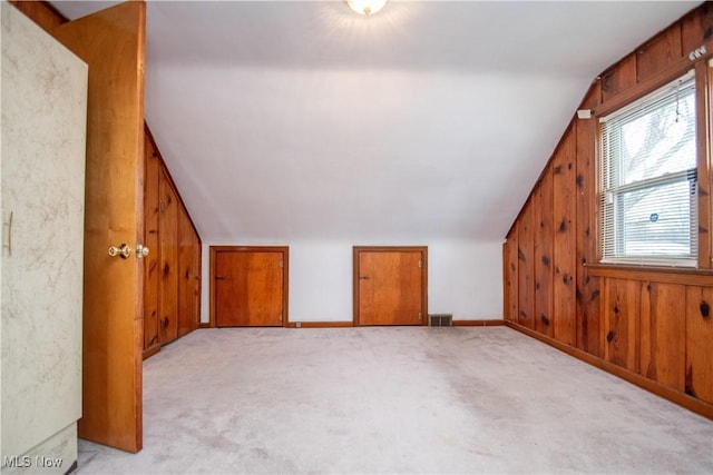 bonus room with wooden walls, light colored carpet, and vaulted ceiling