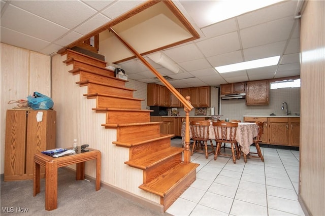 dining room with sink, light tile patterned floors, a paneled ceiling, and wood walls