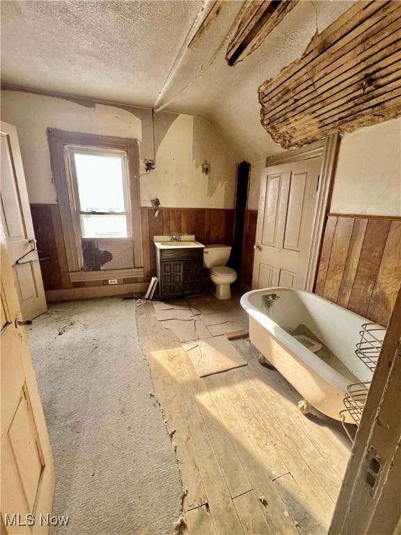 bathroom with hardwood / wood-style floors, a bathtub, a textured ceiling, toilet, and wood walls