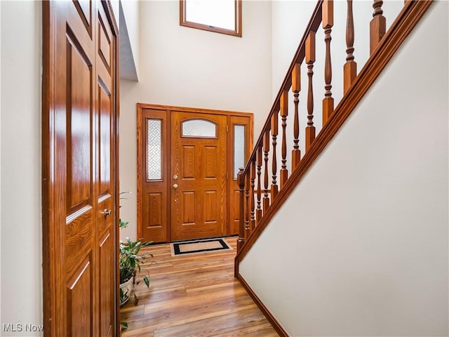 entrance foyer with stairs, a towering ceiling, and light wood finished floors