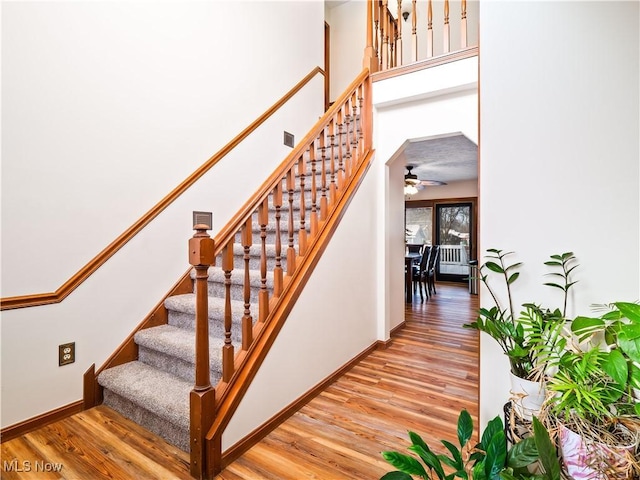 stairs featuring wood finished floors, baseboards, and a towering ceiling