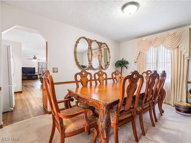 dining space with a textured ceiling, wood finished floors, arched walkways, and ceiling fan