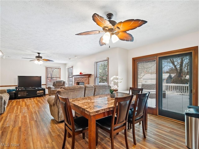 dining space featuring a textured ceiling, hardwood / wood-style floors, a brick fireplace, and a wealth of natural light