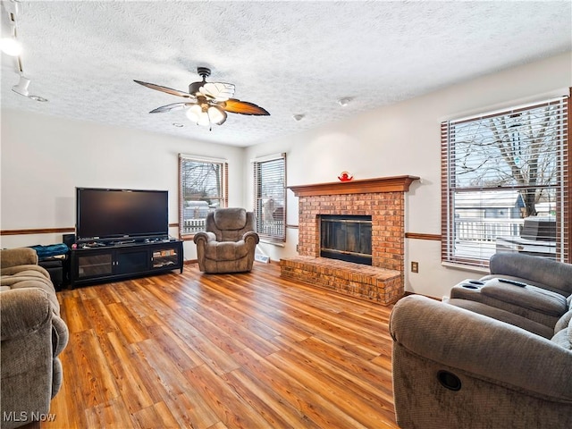 living room with light wood-style floors, a brick fireplace, ceiling fan, and a textured ceiling