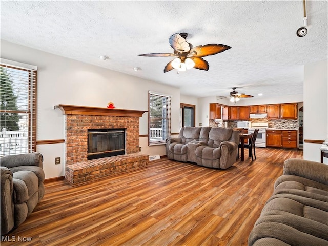 living area with wood finished floors, plenty of natural light, a brick fireplace, and ceiling fan