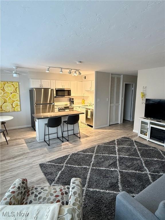 living room featuring ceiling fan, light hardwood / wood-style floors, and a textured ceiling