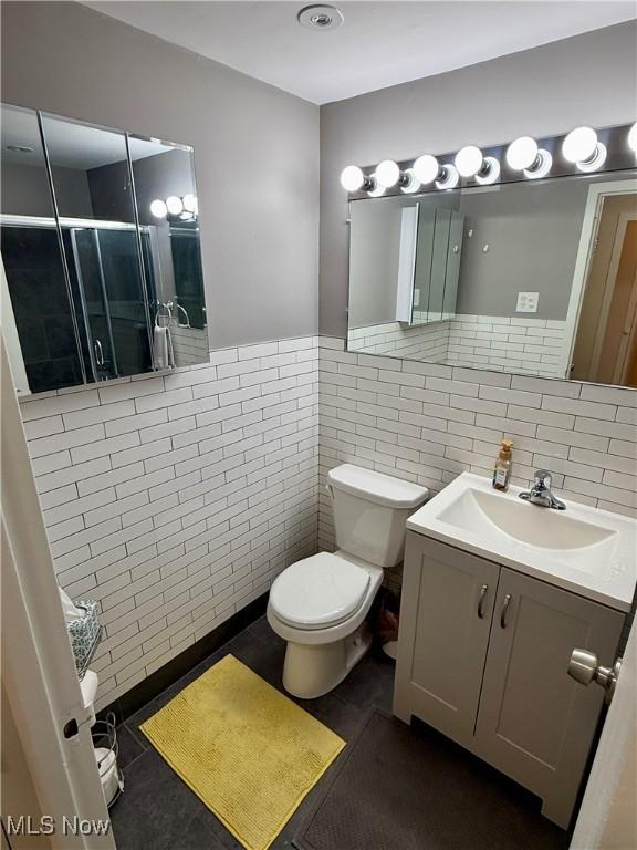 bathroom featuring vanity, toilet, a shower with door, and tile walls