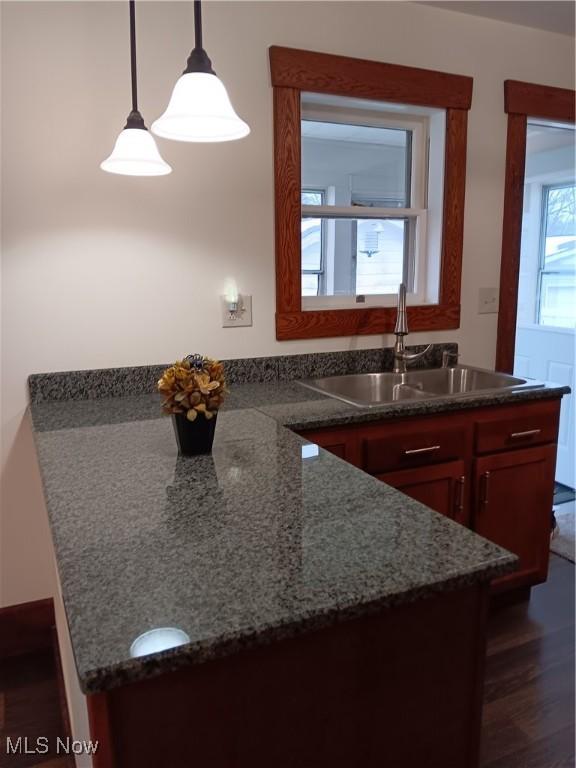 kitchen with sink, decorative light fixtures, dark hardwood / wood-style floors, and dark stone counters