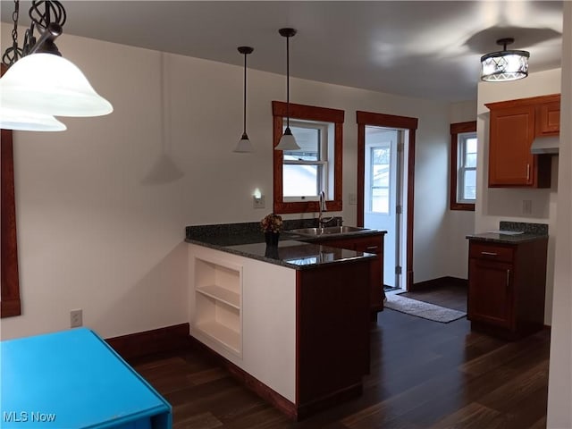 kitchen with sink, hanging light fixtures, dark stone countertops, dark hardwood / wood-style floors, and kitchen peninsula