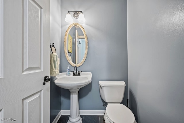 half bath with a sink, baseboards, toilet, and tile patterned flooring